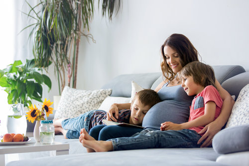 Young pregnant woman, reading book at home to her boys